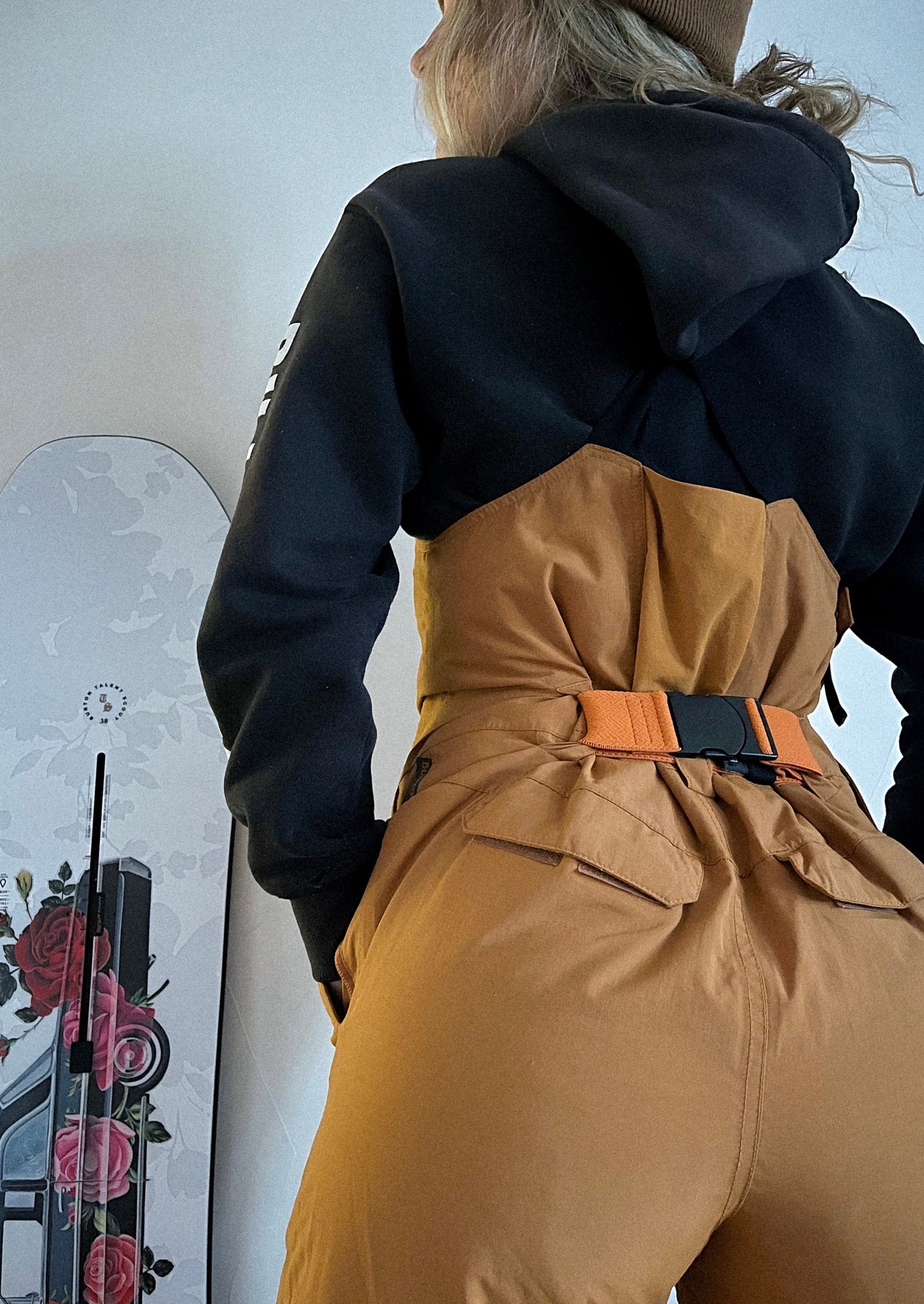 a girl with a snowboard wearing a burnt orange ski bib with an orange bib belt