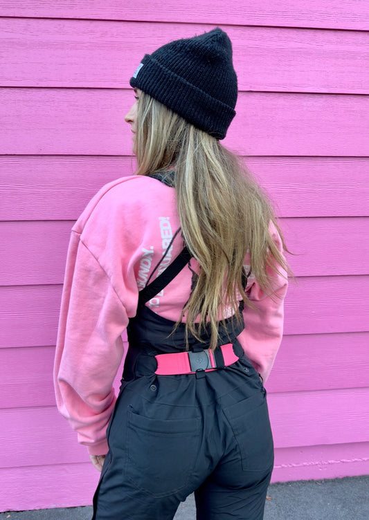 girl standing backwards showing her hot pink bib belt on her ski bibs