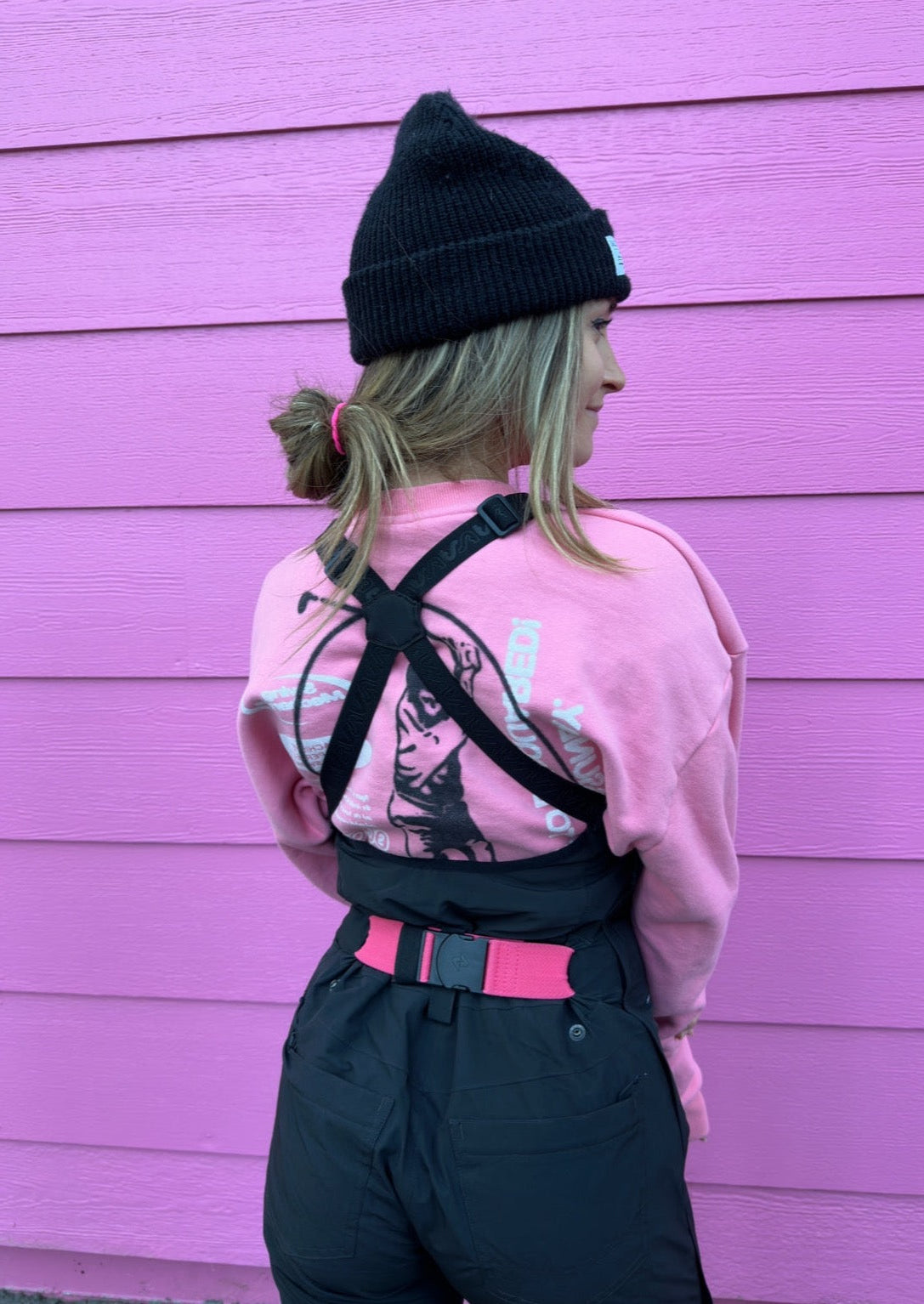 girl wearing a snowboard outfit including a black ski bib and a hot pink bib belt